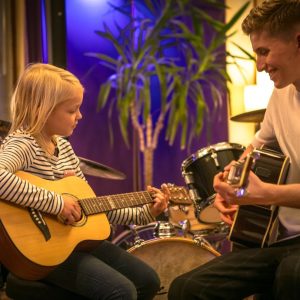 Ein Mann und ein Mädchen spielen Gitarre in einem Musikstudio.